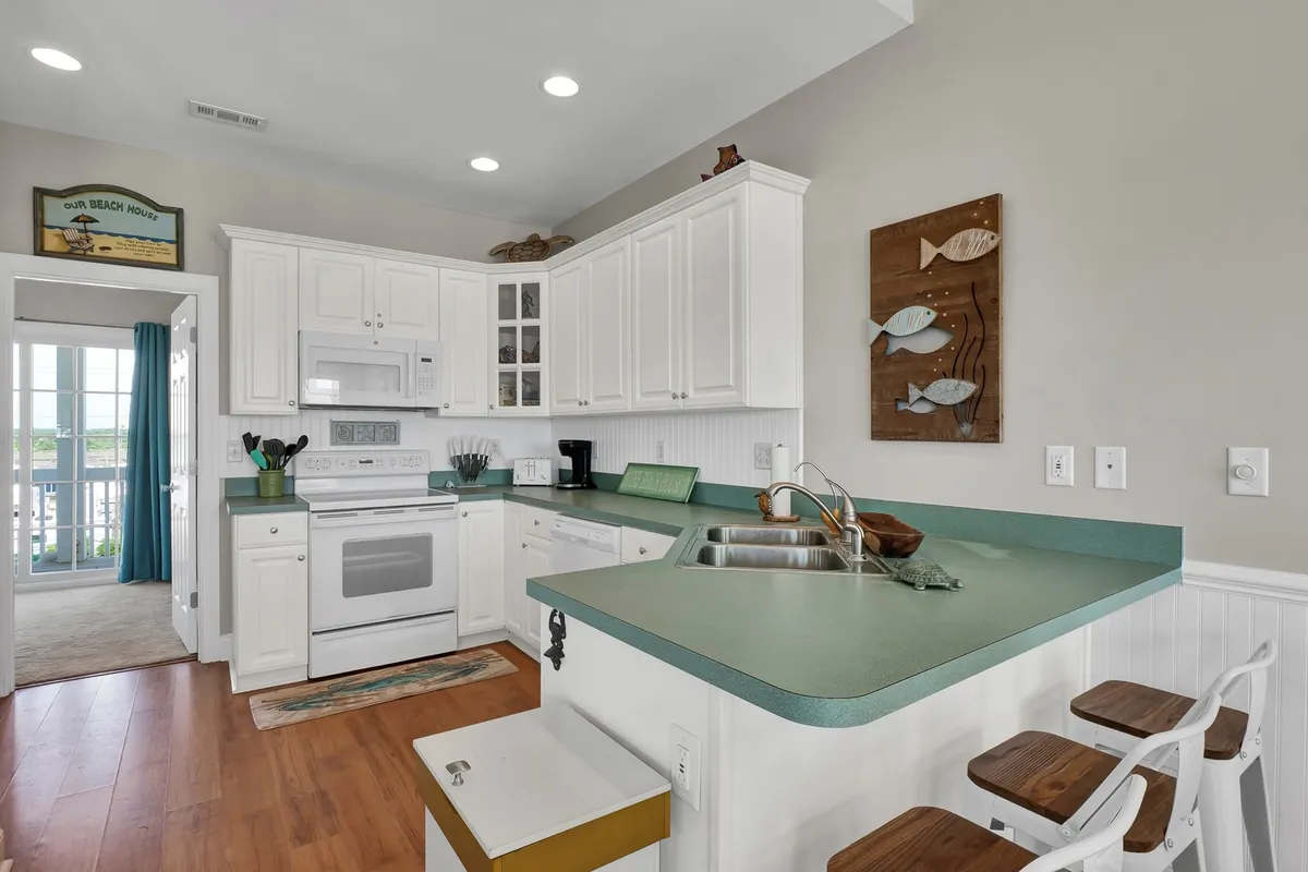 A bright, well-equipped kitchen with a central island, modern appliances, and a window that lets in natural light. Decorative coastal touches and an inviting layout make it ideal for social cooking and family feasts.