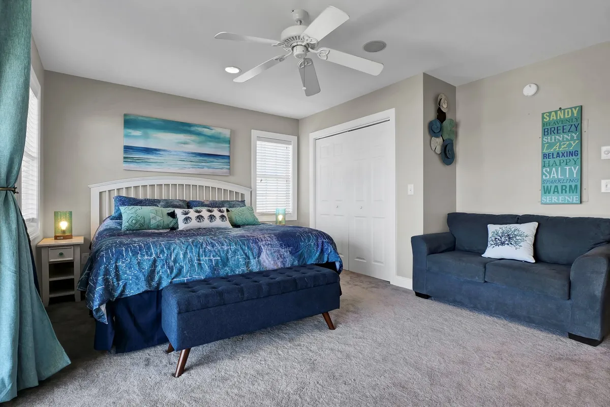 An inviting bedroom interior featuring a bed with blue bedding, ocean-inspired artwork, decorative pillows, a cozy nightstand with lamps, and a sofa, all arranged to create a calm and serene atmosphere ideal for unwinding after a beach day.