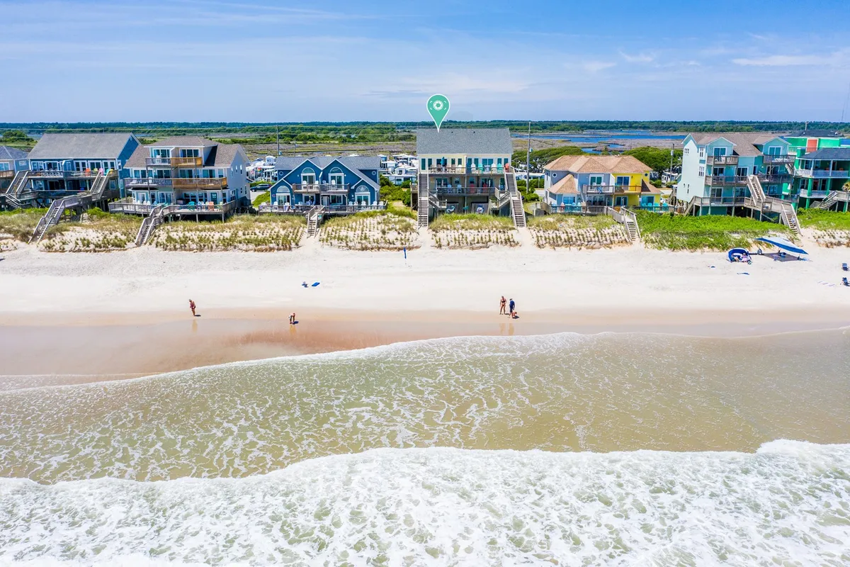 Beachfront houses line the shore, with the sandy beach and ocean waves in the foreground. People can be seen walking on the beach, emphasizing the inviting, tranquil atmosphere and opportunities for leisurely strolls.