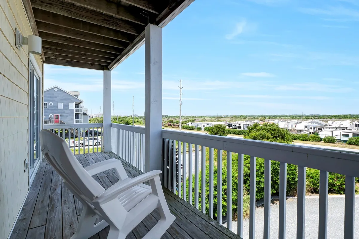 A tranquil balcony scene featuring a rocking chair beside a railing with a distant view of the coastal landscape. The setting sun casts a warm glow, inviting guests to relax, sip coffee, or share a glass of wine while taking in the natural beauty.