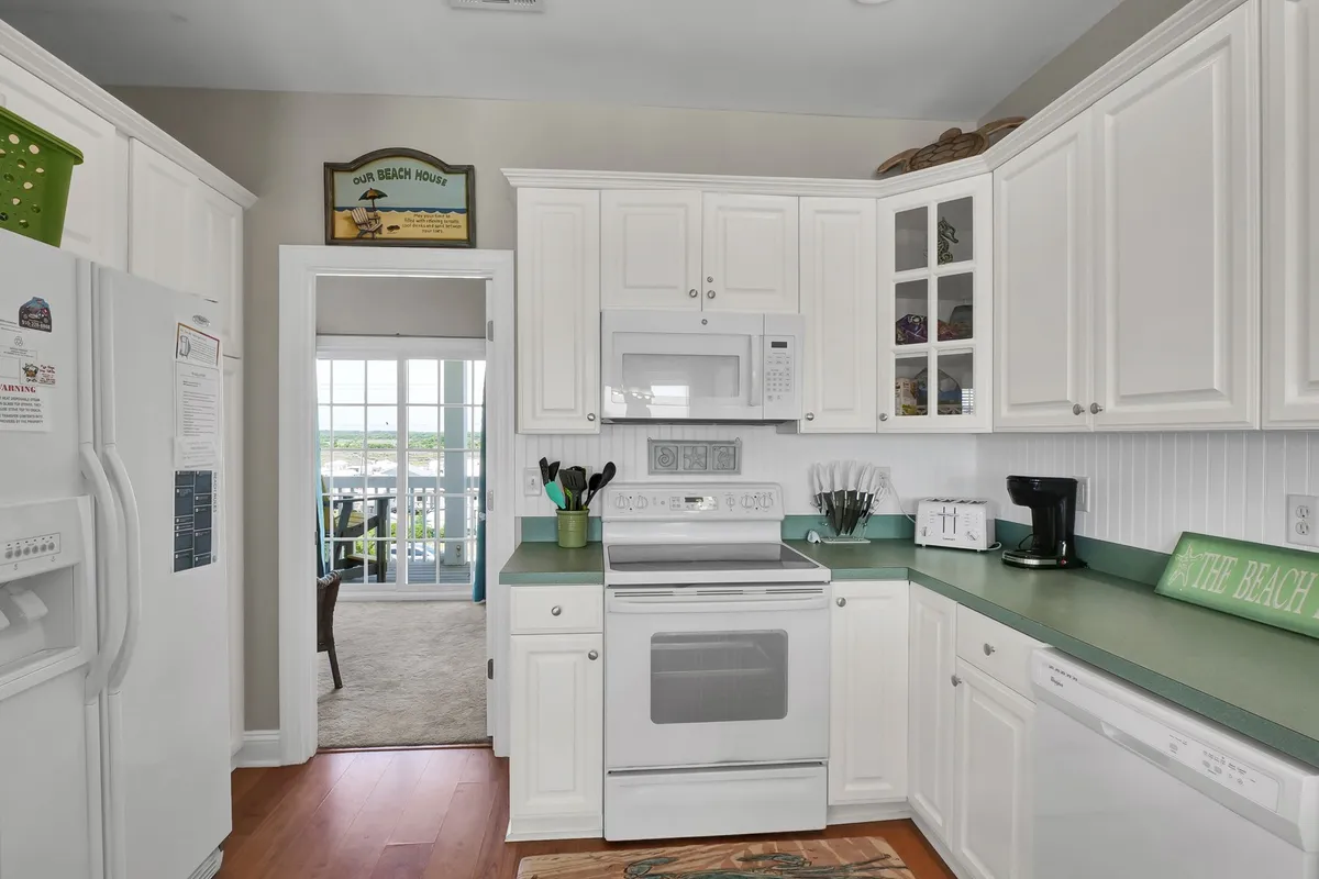 This image showcases a bright kitchen featuring green countertops, white cabinetry, and beach-themed decor. Modern appliances are visible, providing a sense of the home's functionality and contemporary conveniences. Natural light fills the space, making it feel welcoming for family gatherings and meal preparation.