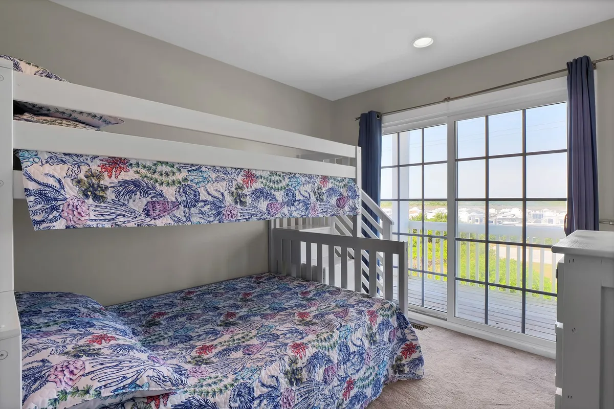A playful and welcoming bunk room with twin and full-size beds, vibrant bedding, a large window, and unique textile patterns, capturing a space designed for kids, teens, or extra guests to sleep, play, and bond.
