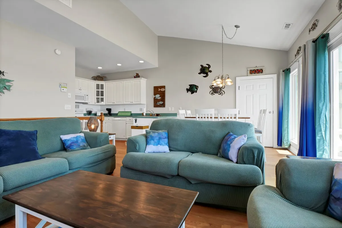 A spacious, relaxed living room with comfortable sofas, a wooden coffee table, and an open view into the kitchen area—an inviting space for family gatherings, casual conversations, or accommodating extra guests with the sleeper sofa.