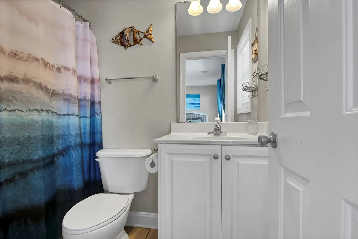 A calm, serene bathroom with a shower curtain in ocean hues, fishing-themed wall decor, and clean white cabinetry—an inviting spot for refreshing after beach adventures, with plenty of space for families to get ready.